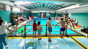 An indoor swimming pool with a diving board, multiple lanes, and a spectator area.
