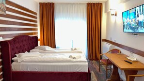 Une chambre d’hôtel avec un grand lit, un bureau, une chaise et un téléviseur fixé au mur.