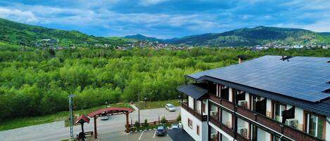 Ein Hotel mit Solaranlage auf dem Dach, Parkplatz und Blick auf ein grünes Tal.
