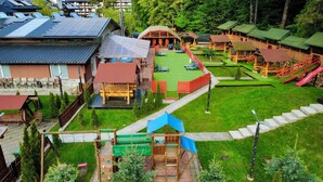 A playground with slides and swings, surrounded by green lawns and wooden structures.