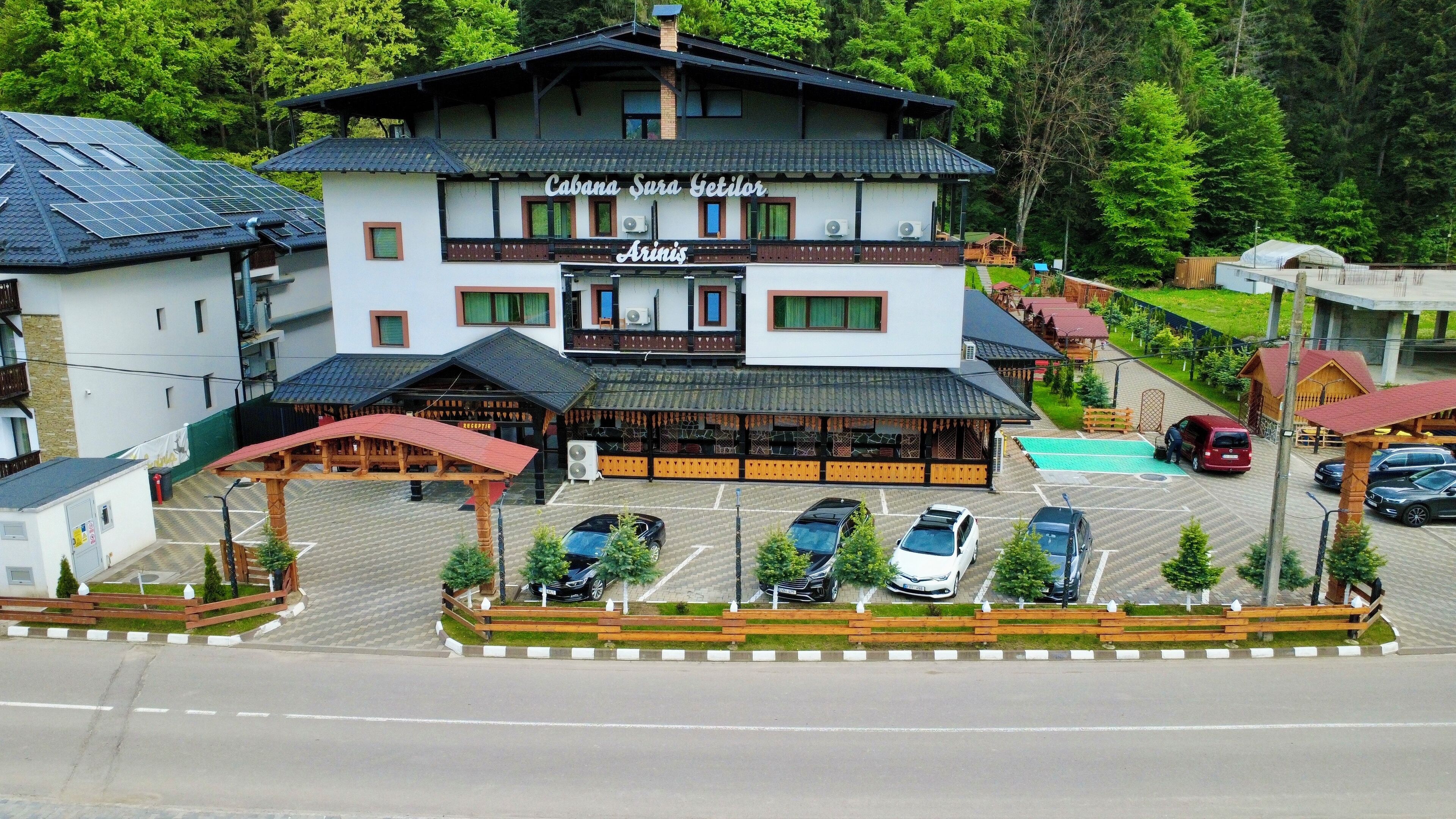 A hotel with a central building, a parking area, and a pool.