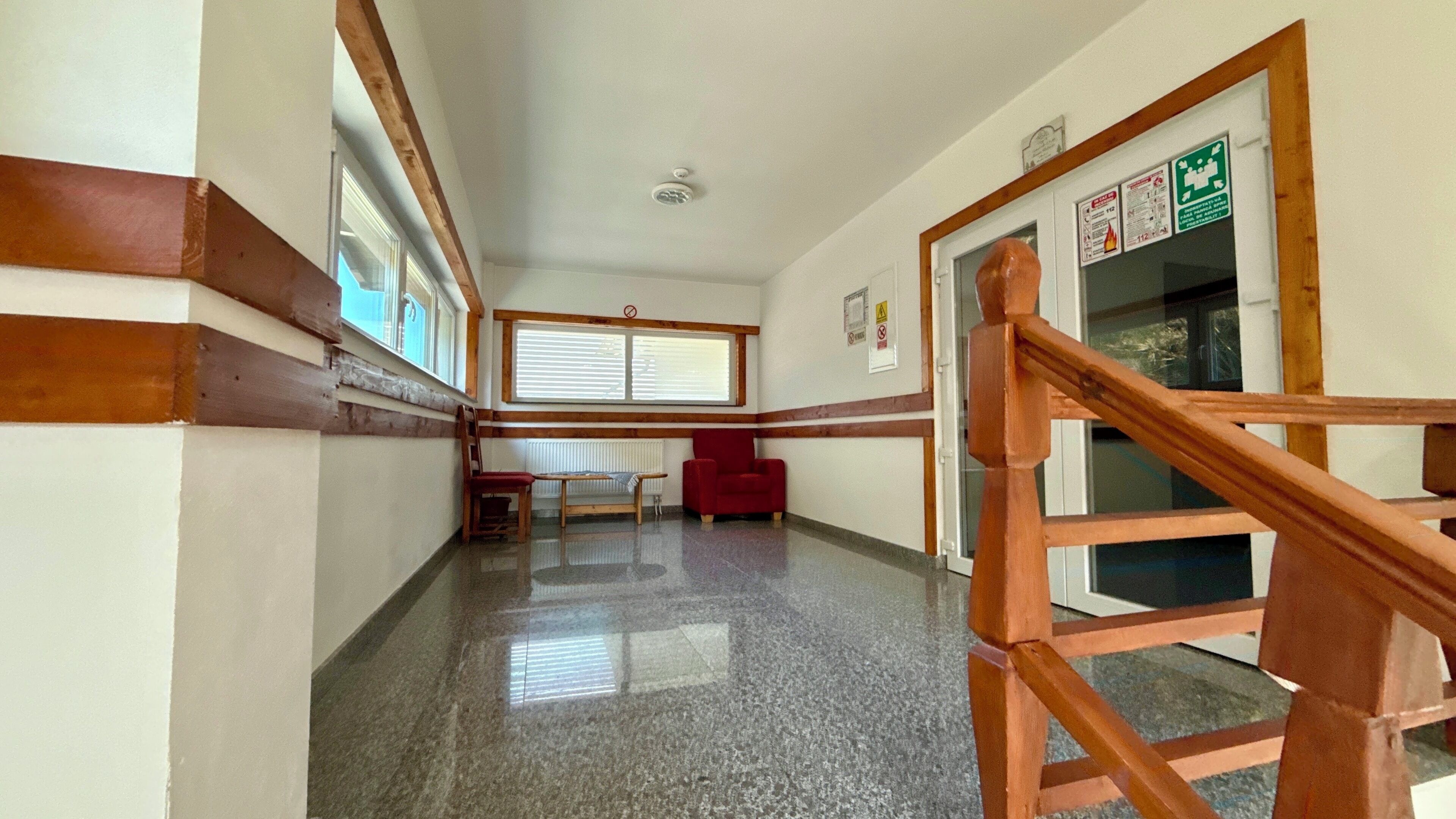 Un pasillo con suelo pulido, detalles de madera, una silla roja, un banco de madera y una escalera con barandilla de madera.