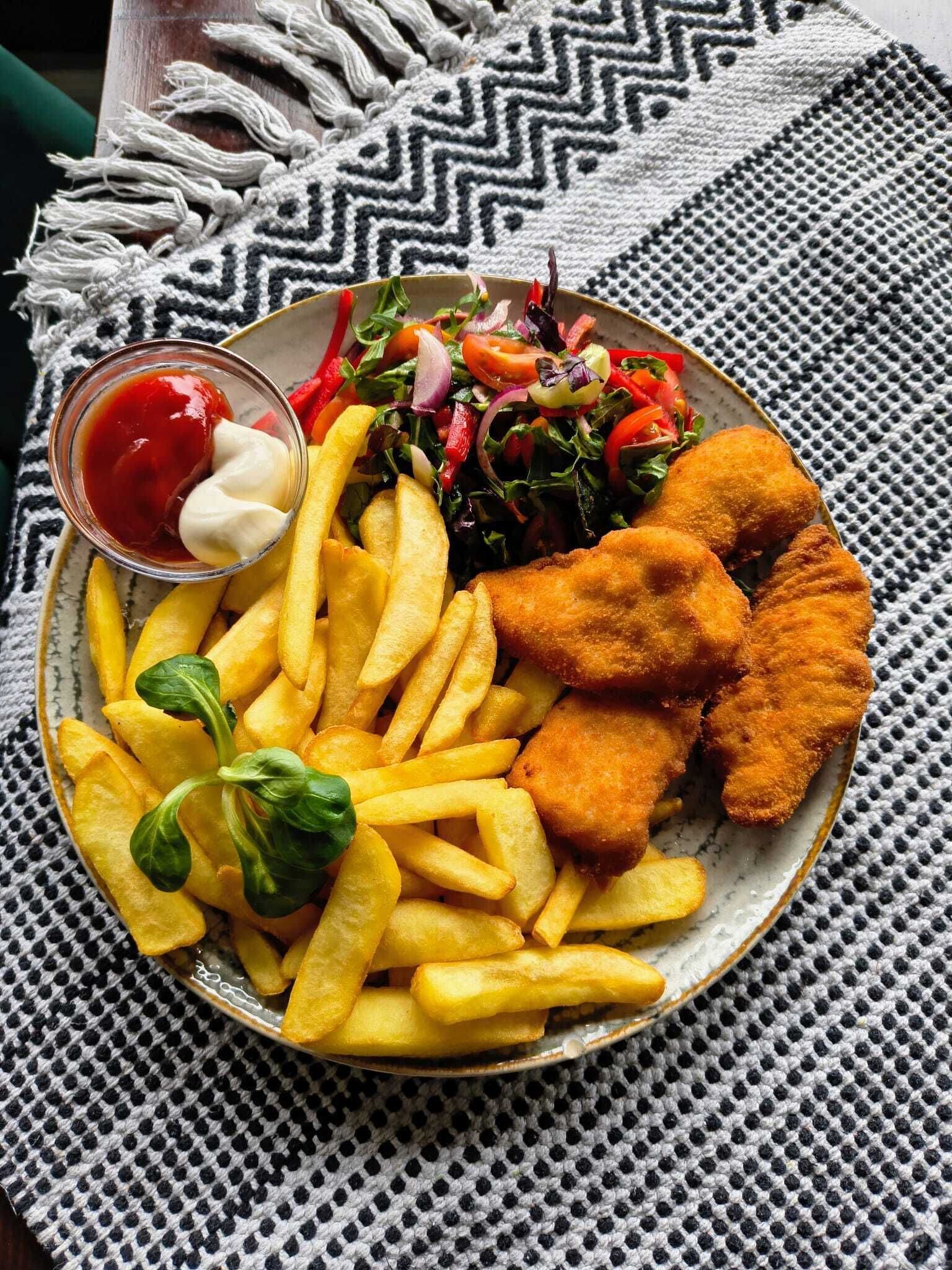 A plate of food including fried fish, French fries, a salad, and a small bowl of ketchup.