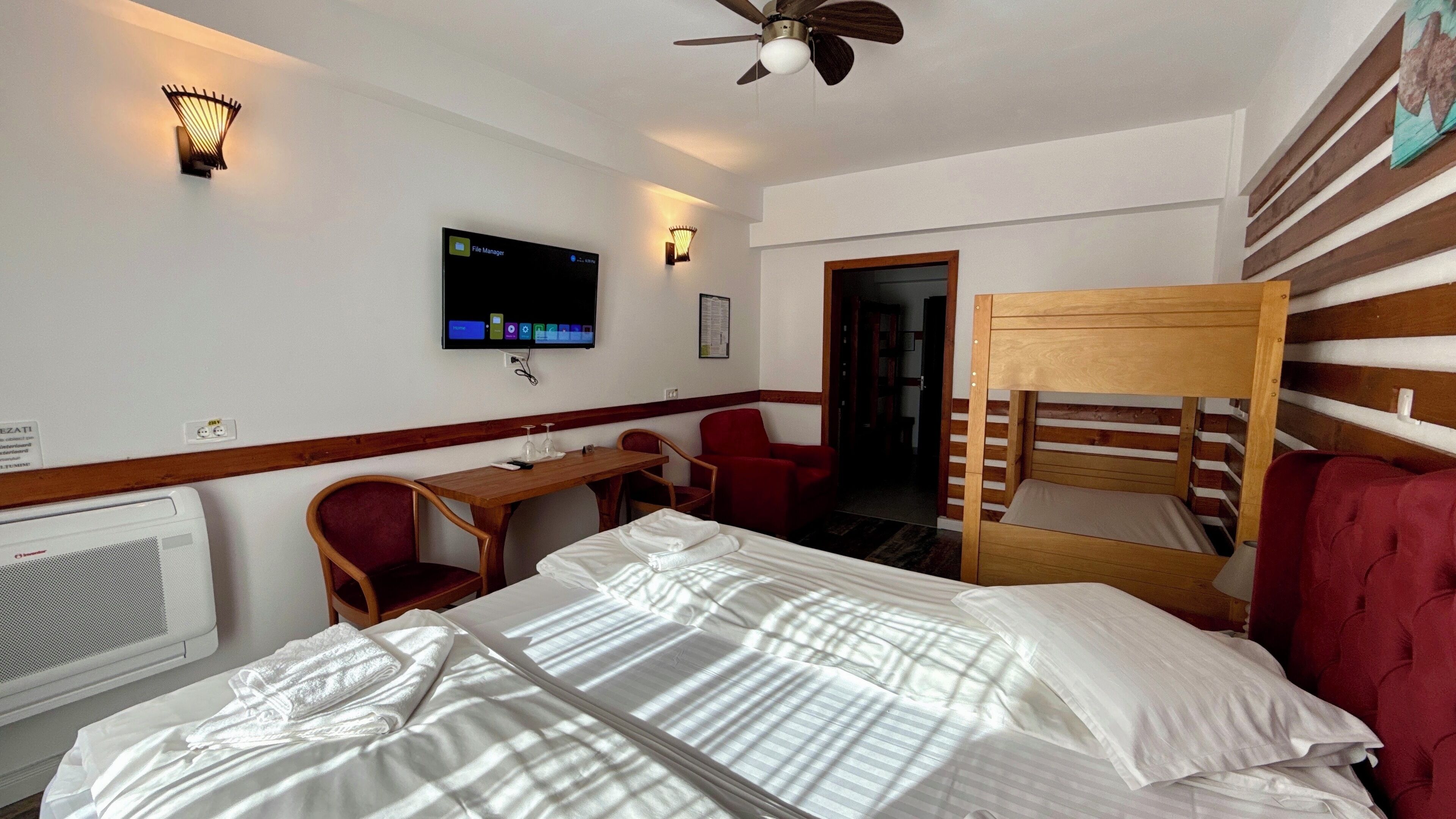 A hotel room with a bed, a desk, a chair, a TV mounted on the wall, and a ceiling fan.