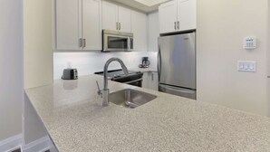 Eine moderne Küche mit weißen Schränken, Edelstahlgeräten, einer Granitarbeitsplatte und einer eingebauten Mikrowelle.