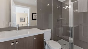 A modern bathroom with a glass-enclosed shower, a white sink, and a toilet.
