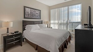 A hotel room with a large bed, a desk with a lamp, a television, and a window with blinds.