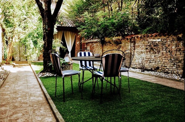 Relax in a shaded outdoor space surrounded by trees, with a brick wall, seating area, and well-maintained lawn.