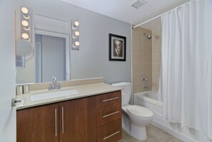 A bathroom with a vanity, sink, mirror, lights, toilet, bathtub, and shower curtain.