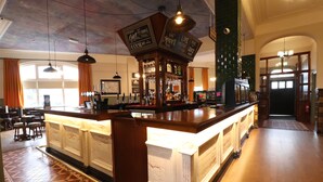 A bar area with a wooden counter and hanging lights. There are bar stools and a large window with curtains. - The Bridge Hotel (Bolton)