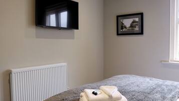 Un dormitorio con una cama, un televisor montado en la pared, un cuadro enmarcado y un radiador.