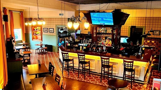 A bar area with a counter, multiple stools, and tables. - The Bridge Hotel (Bolton)
