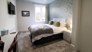 A bedroom with a bed, bedside table, lamp, and a window with curtains. - The Bridge Hotel (Bolton)