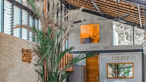 Una sala de estar moderna con un sofá gris, cojines estampados, una mesa de centro tejida y una planta grande.
