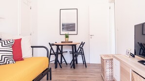 A compact room with a bed, a small table with chairs, a TV, and a framed picture on the wall. - Bairro Conqvistador Apartment 4 (Lisboa)