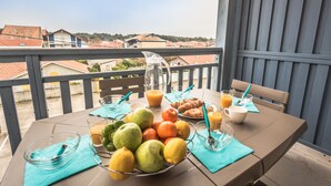 A balcony table with a fruit bowl, croissants, orange juice, and a pitcher.