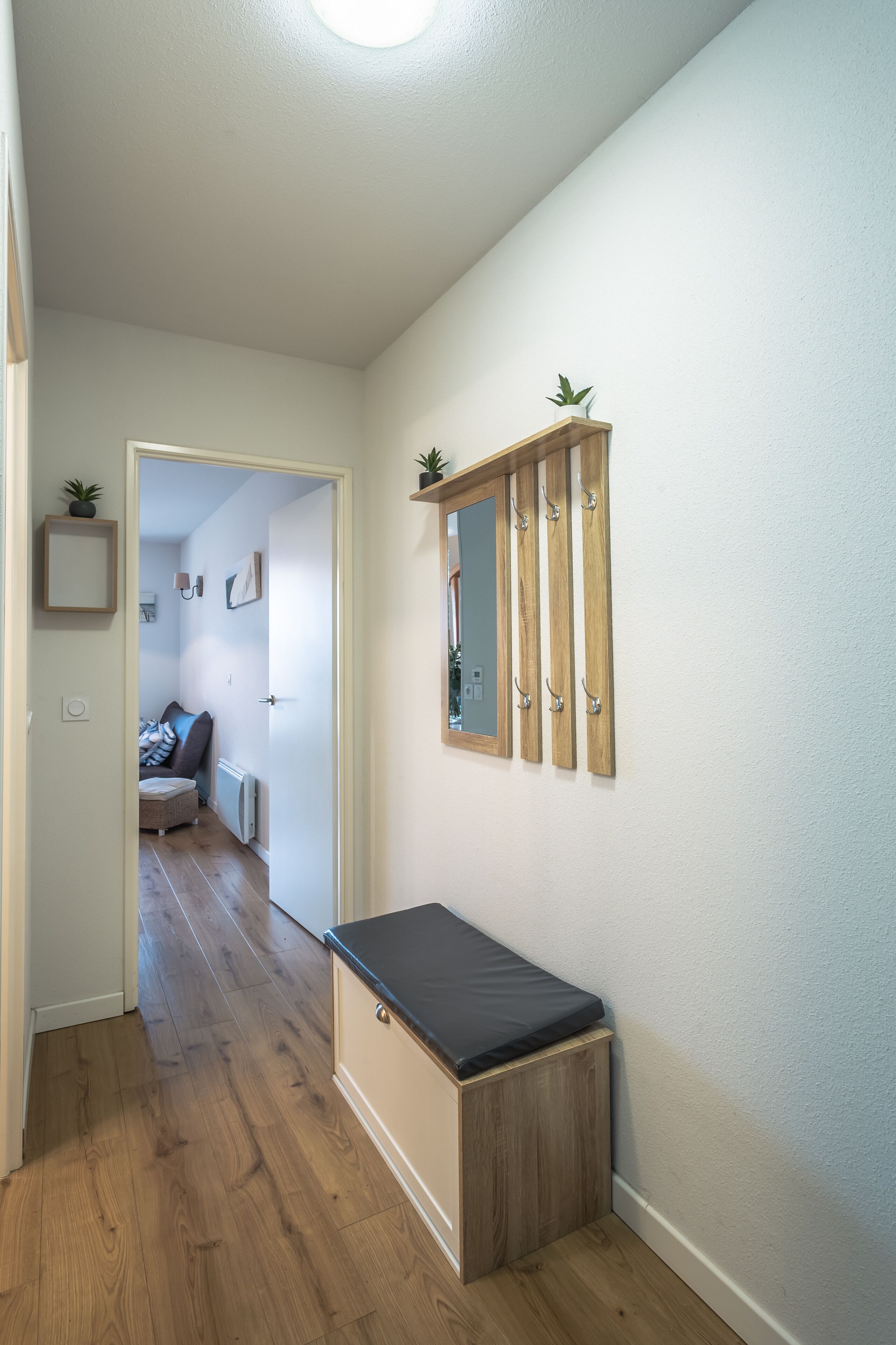 Un corridoio con pavimento in legno, una panca, uno specchio e una porta che dà su una camera da letto.