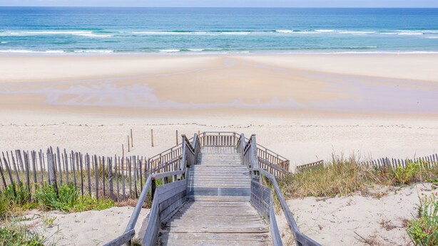 A wooden boardwalk leading to a sandy beach with ocean views.