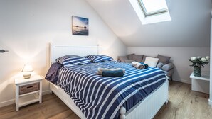 A bedroom with a bed, bedside table, lamp, and a window with a view of the sea.
