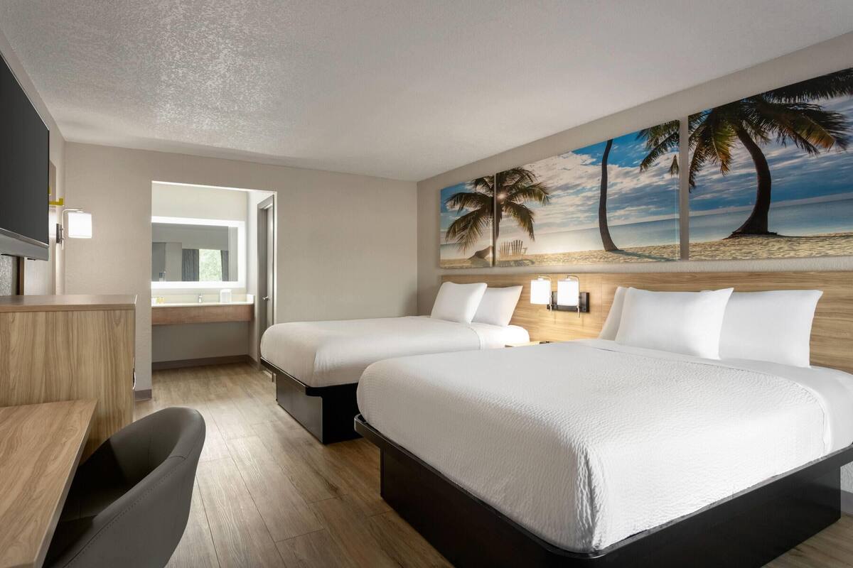 A hotel room with two beds, a desk, and a TV.