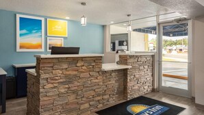 A reception area with a stone counter, framed pictures on the wall, and a view of the outside through glass doors. - Days Inn by Wyndham Apopka/Orlando (Apopka)