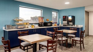 A compact kitchen with a blue wall, a microwave, a coffee machine, and a toaster. There are wooden tables and chairs. - Days Inn by Wyndham Apopka/Orlando (Apopka)