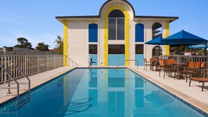 A swimming pool with a sun terrace, a Days Inn sign, and a building with yellow and blue accents. - Days Inn by Wyndham Apopka/Orlando (Apopka)