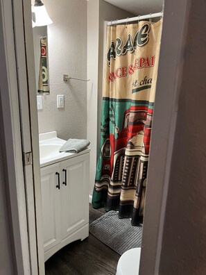 Une salle de bain avec un lavabo blanc, un miroir et un rideau de douche orné d’un motif représentant un véhicule.