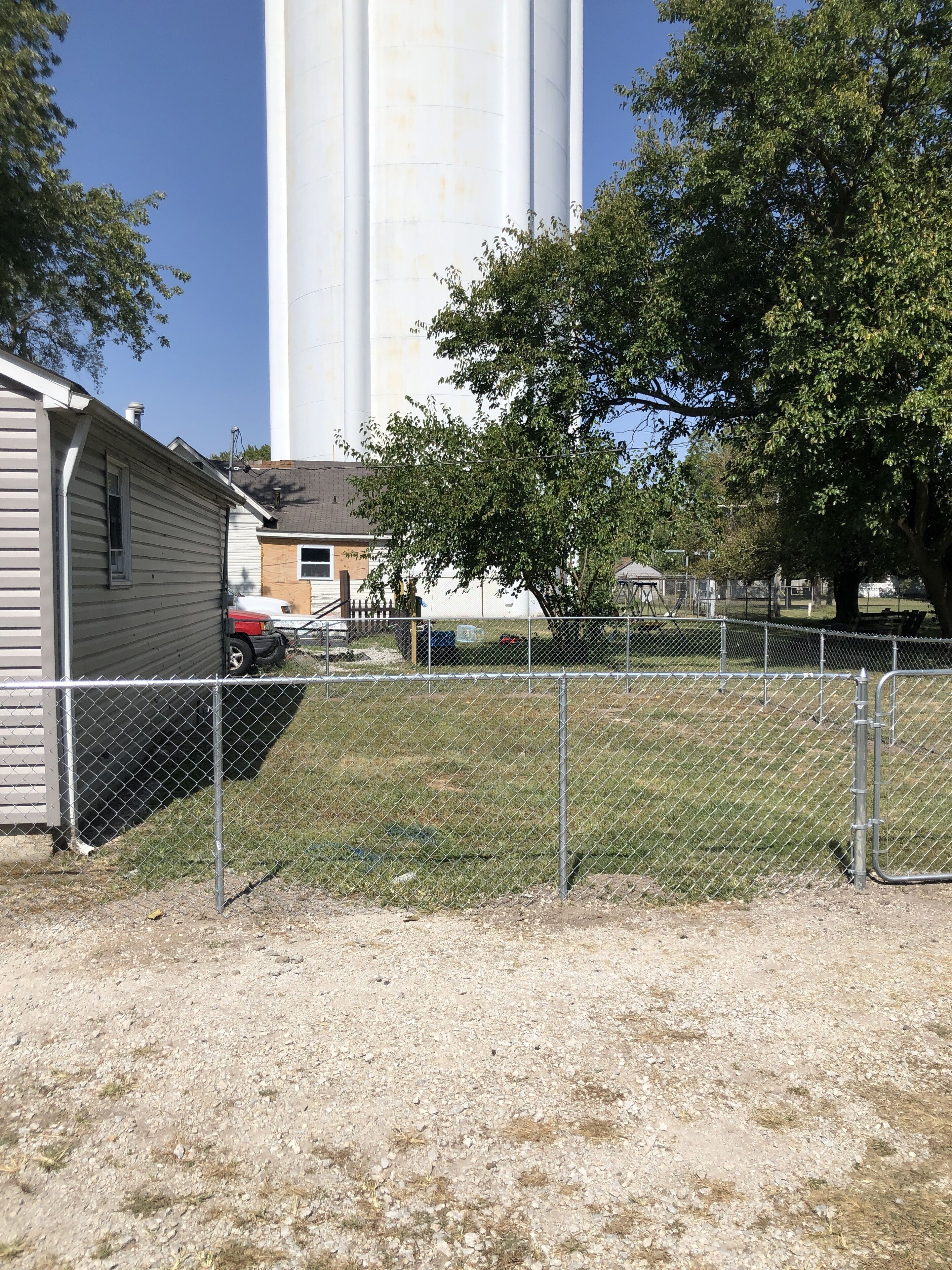 A fenced area with a building, a tree, and a large white structure in the background.
