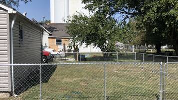A fenced area with a building, a tree, and a large white structure in the background.