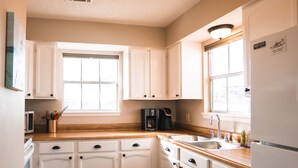 Una cocina con armarios blancos, encimera de madera, cafetera y refrigerador.