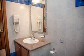 A bathroom with a sink, mirror, towel dispenser, and toilet paper holder.