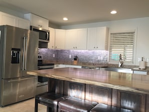 Una cocina moderna con electrodomésticos de acero inoxidable, encimera de granito y taburetes de bar de madera.