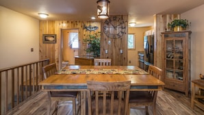 A wooden dining room with a large clock, wooden chairs, and a wooden table.