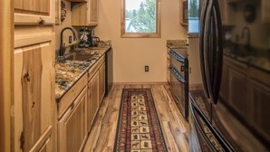 A kitchen with wooden cabinets, a granite countertop, a window, and a refrigerator.