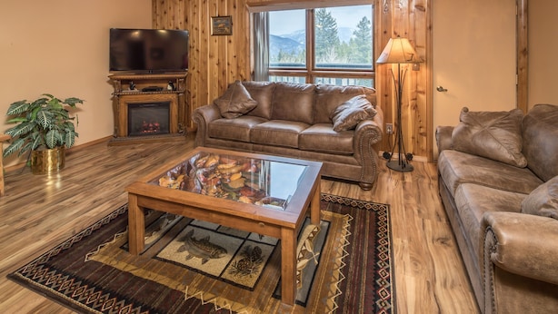 A cozy living room with a fireplace, leather sofas, a glass coffee table, and a television.