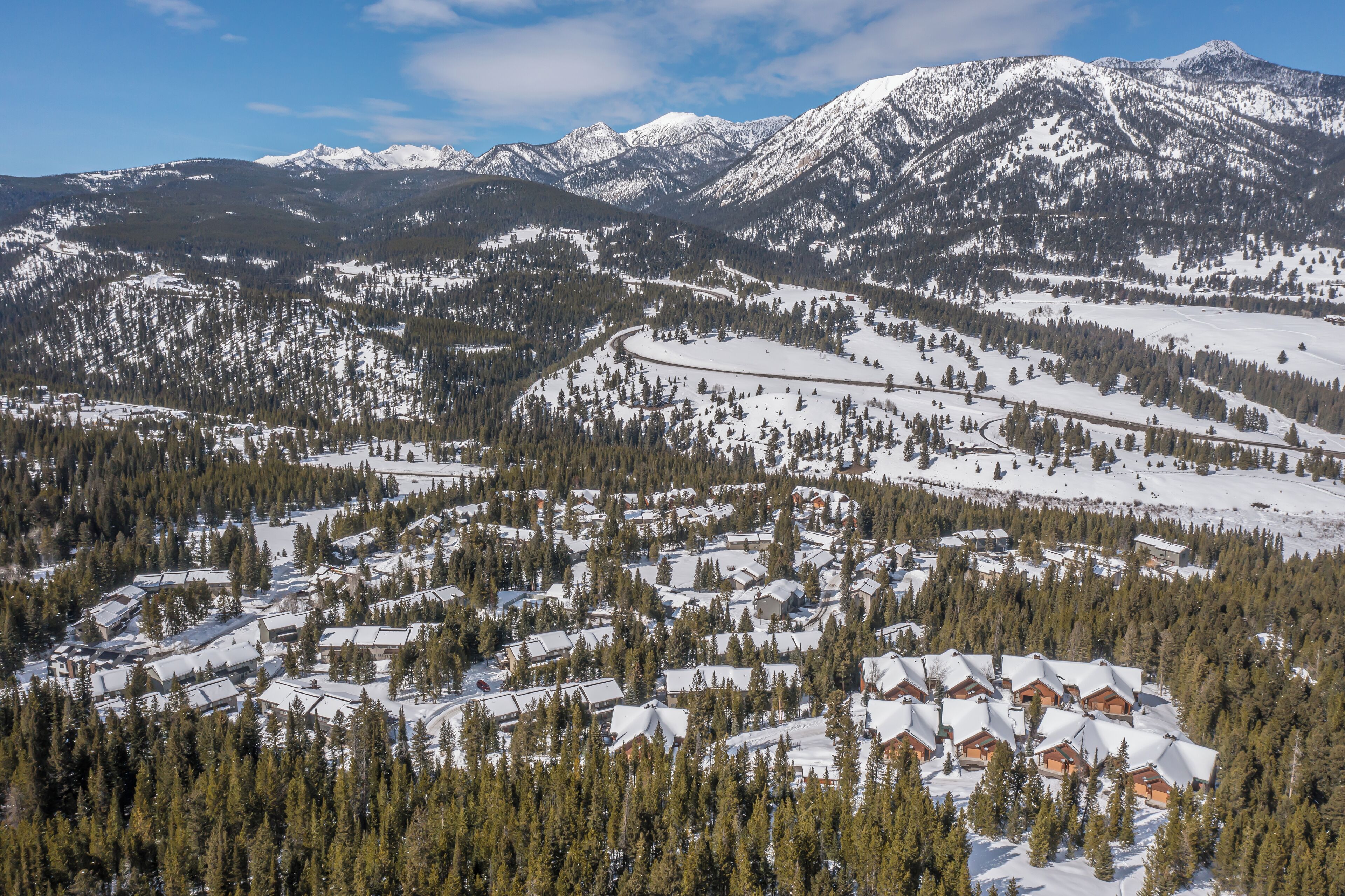 A snow-covered mountain landscape with a cluster of cabins surrounded by dense forests.