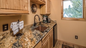 A kitchen with wooden cabinets, a granite countertop, a sink, and a window with a view of trees.