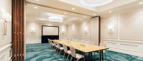 A conference room with a long table, chairs, and a large wooden panel on the left.