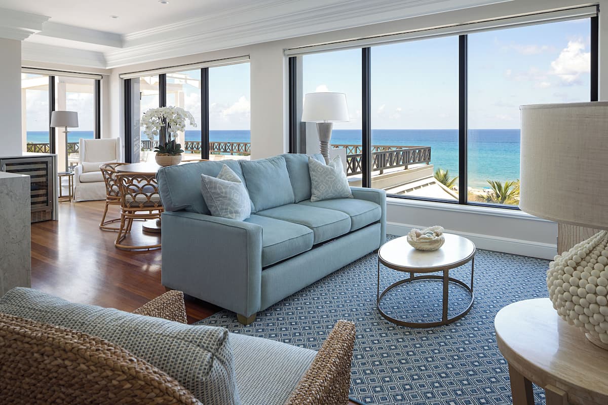 Amplia sala de estar con un gran ventanal que ofrece vistas al océano, un sofá cómodo, un comedor y una lámpara decorativa.