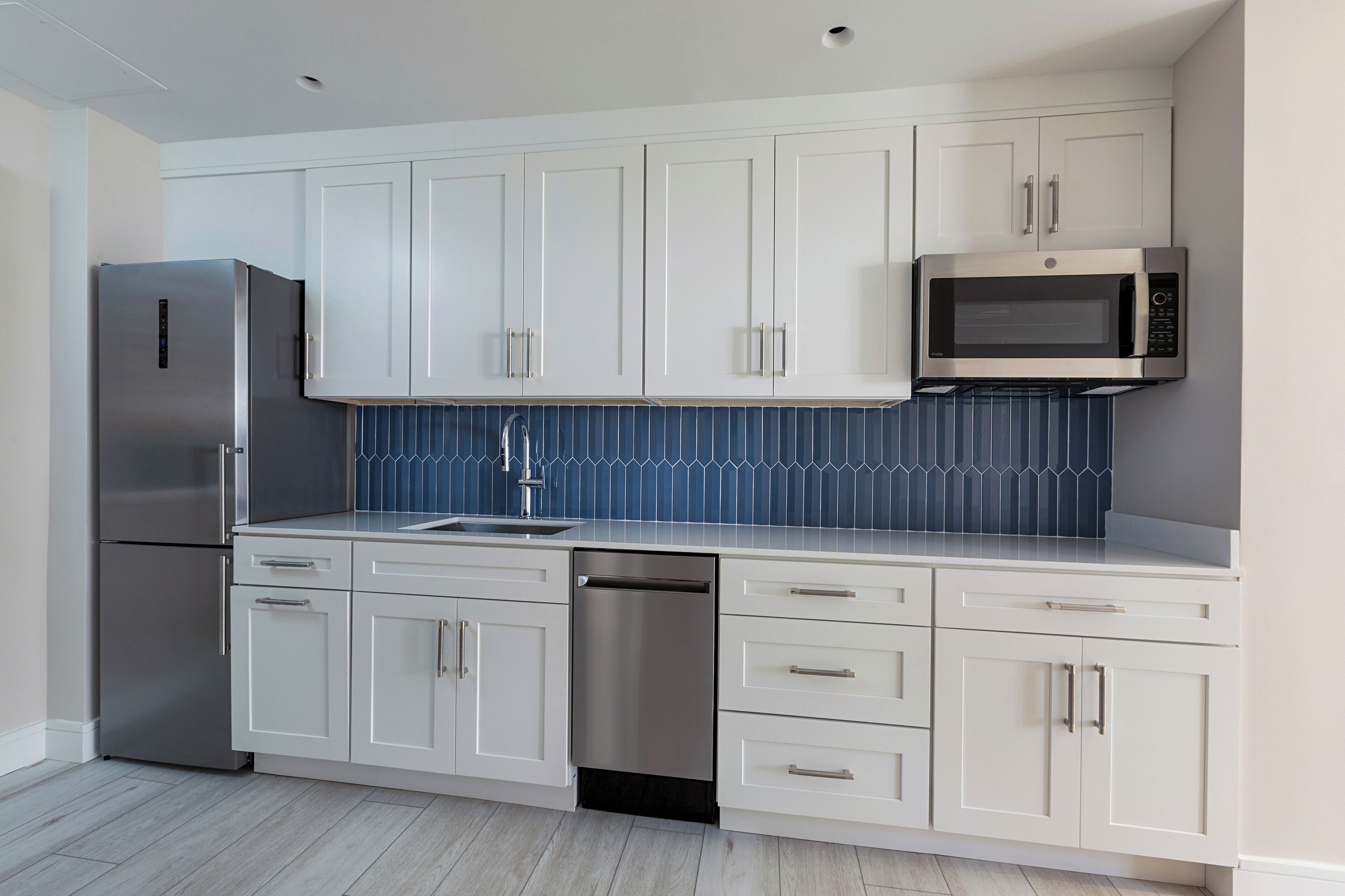 A modern kitchen with white cabinets, a stainless steel refrigerator, a dishwasher, and a microwave.