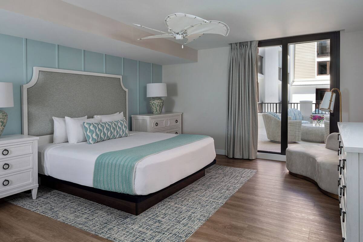 Un dormitorio con una cama grande, mesitas de noche, ventilador de techo y vistas al balcón exterior.