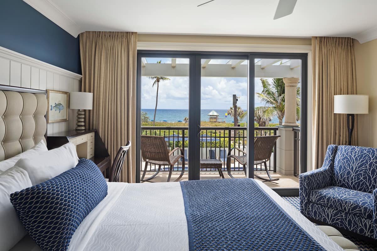 Habitación de hotel con cama, dos sillas, una mesa y vista al océano.