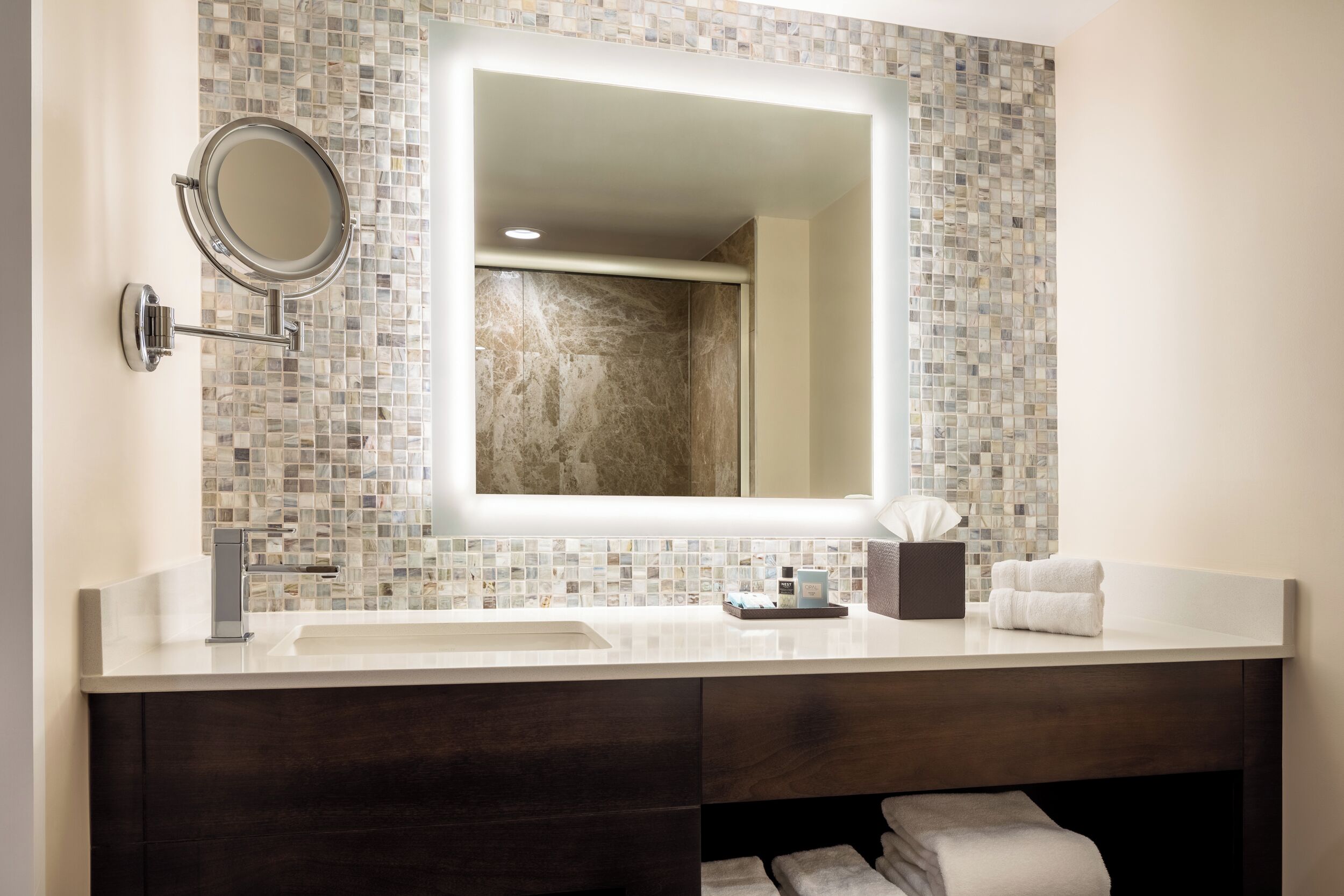 A modern bathroom with a large mirror, two sinks, and a dark wood vanity.