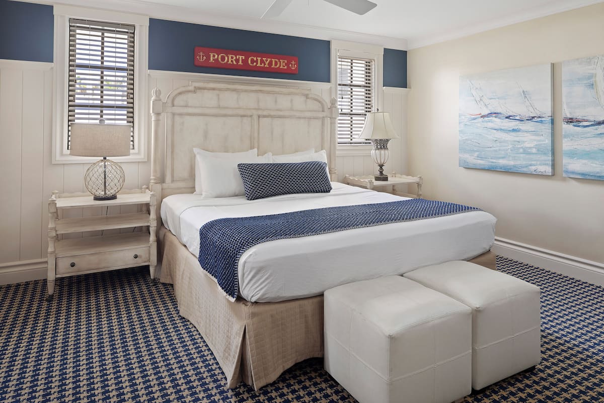 Un dormitorio con una cama grande, una mesita de noche, un banco y un cartel en la pared que dice "Port Clyde".