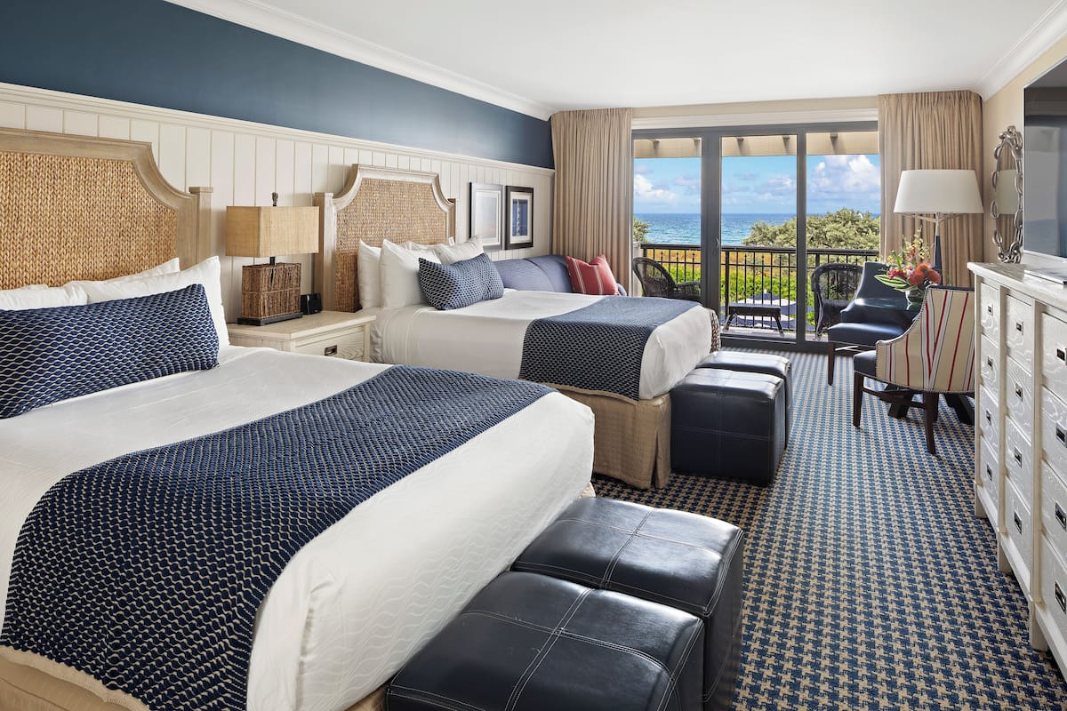Habitación de hotel con dos camas, un escritorio y vista al océano.