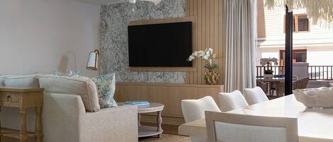 A modern living room with a flat-screen TV mounted on a marble wall, a beige sofa, a dining table with chairs, and a ceiling fan.