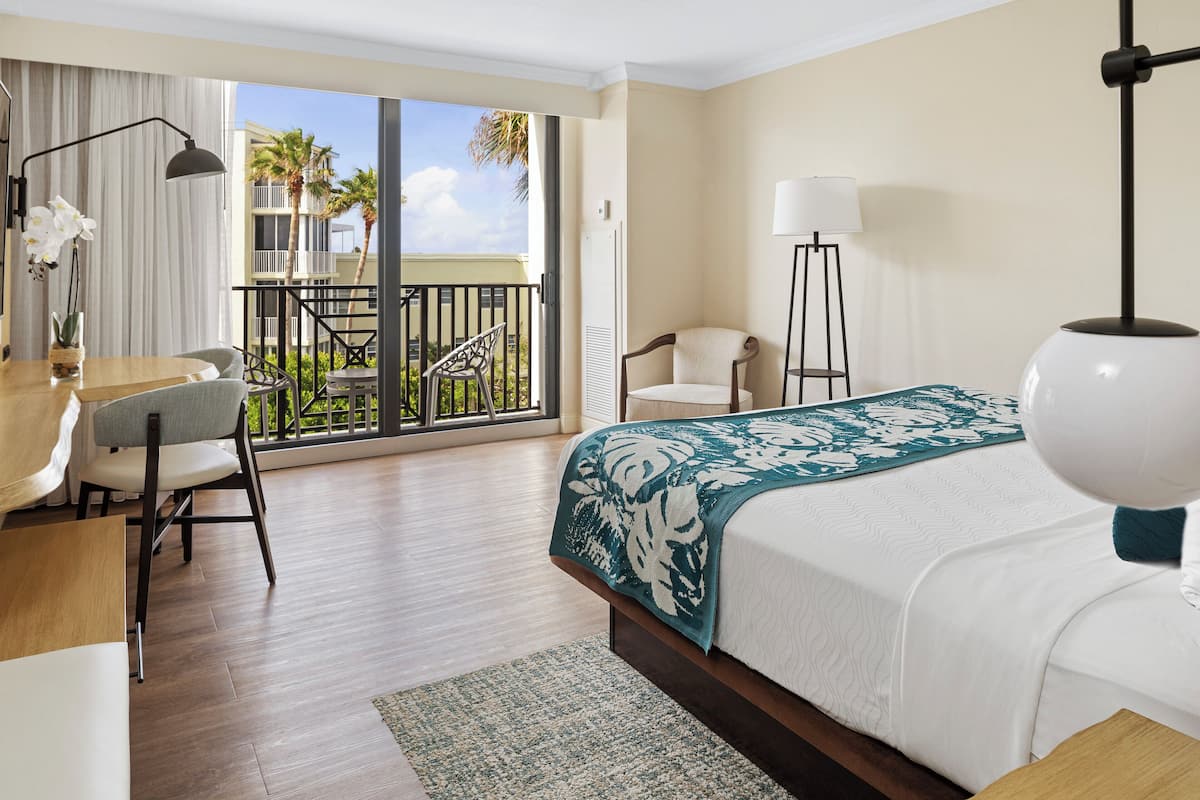Habitación de hotel con cama, escritorio, silla, lámpara y vistas al exterior.