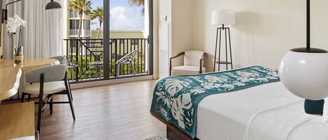 A hotel room with a bed, a desk, a chair, a lamp, and a view of the outdoors.