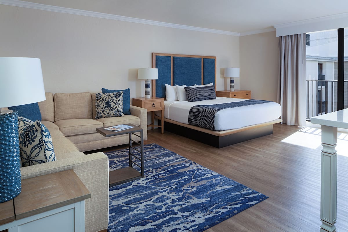 Habitación de hotel con cama, sofá, mesa de centro y vistas al exterior.